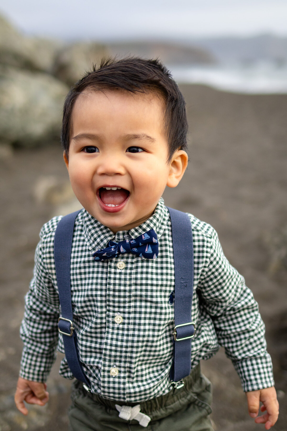 Smiling toddler in suspenders laughing on the beach during Bay Area school photography lifestyle session – Ellobelle Photography