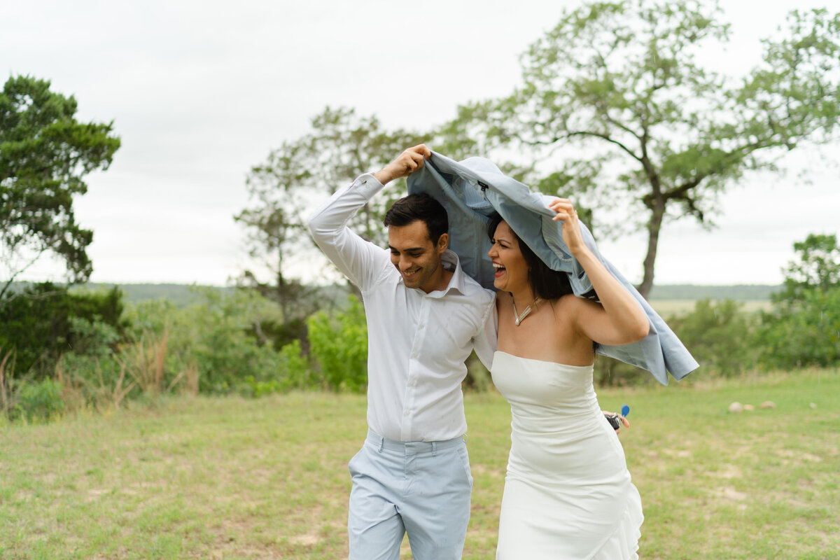a couple holds a suit jacket over them and runs to the vehicle as it rains