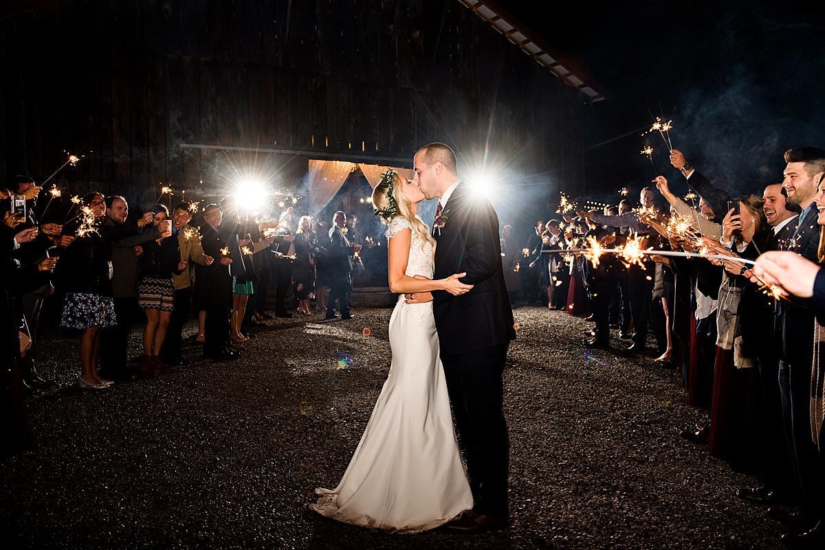 Couple kissing at the end of the night during their sparkler exit with the barn at Drakewood Farm behind them