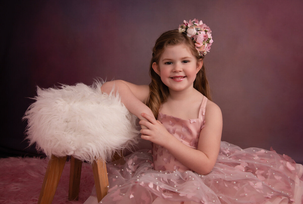 girl-sitting-in-studio-with-pink-butterfly-gown-leaning-on-white fuzzy-stool-arlington-tx