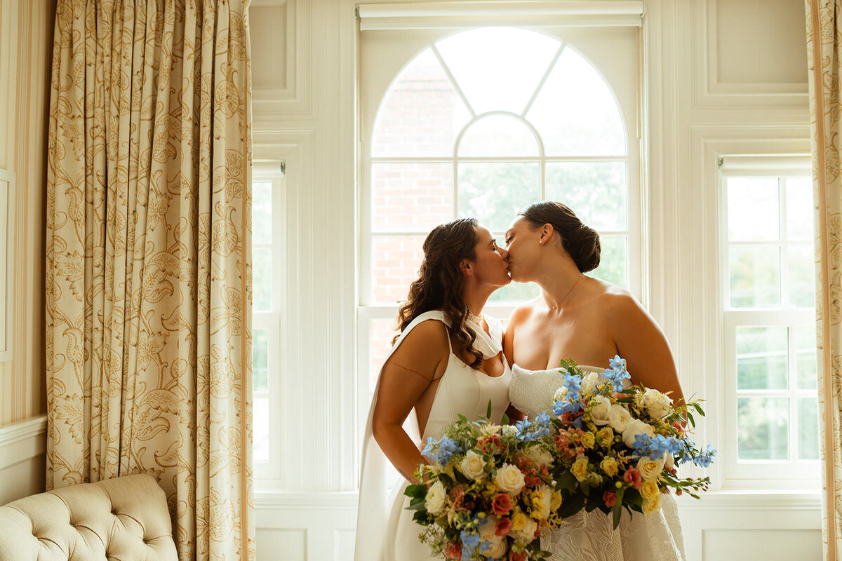 Two brides kissing while holding their wedding bouquets