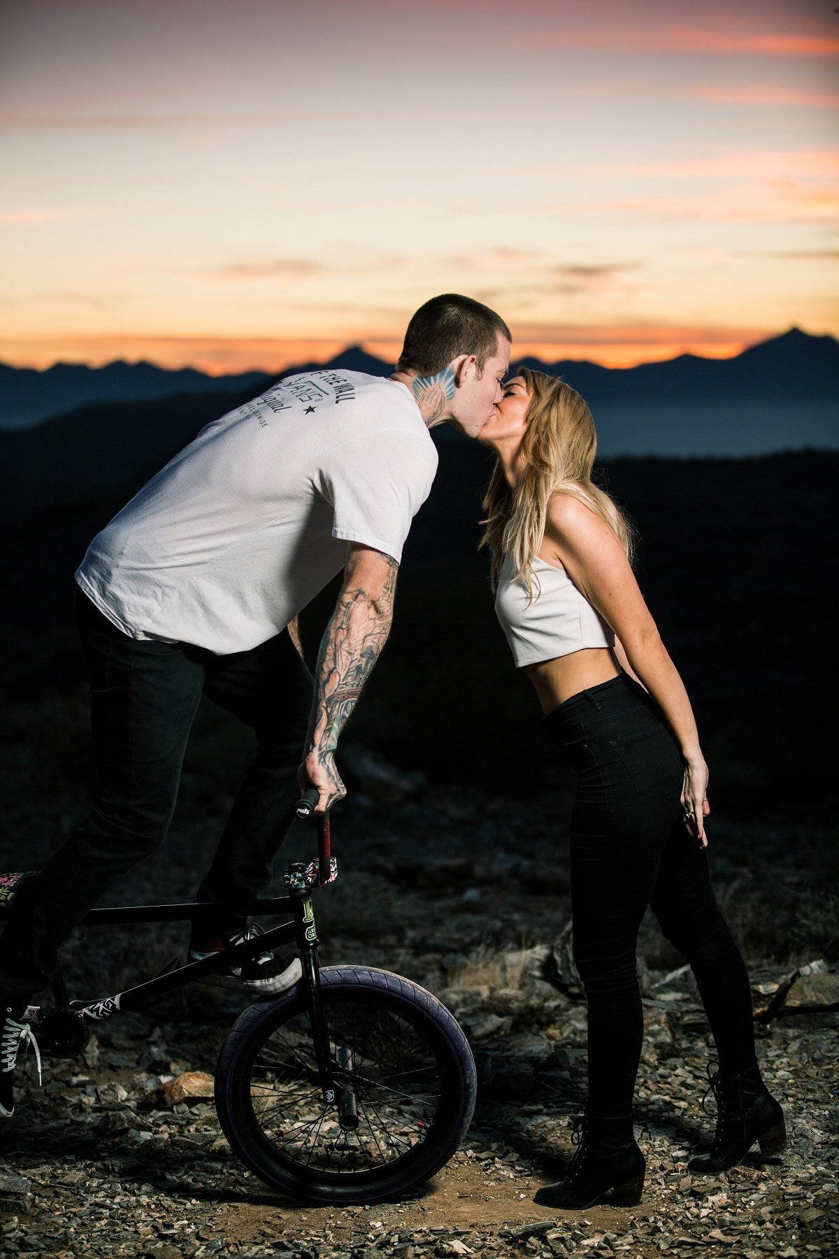 Groom to be stands over his bike and leans in for a kiss from his fiance