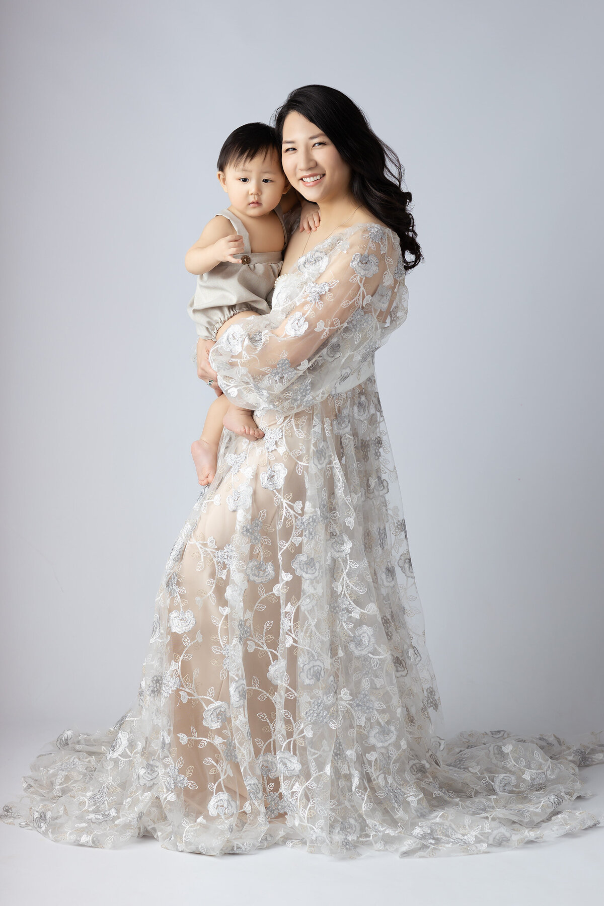 Dallas baby milestone photographer captures a mother and son, smiling warmly in a floral gown, during a tender moment.