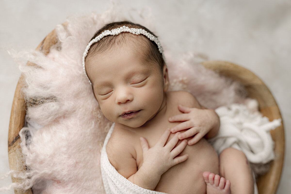 newborn baby girl with hands on chest laying in heart basket