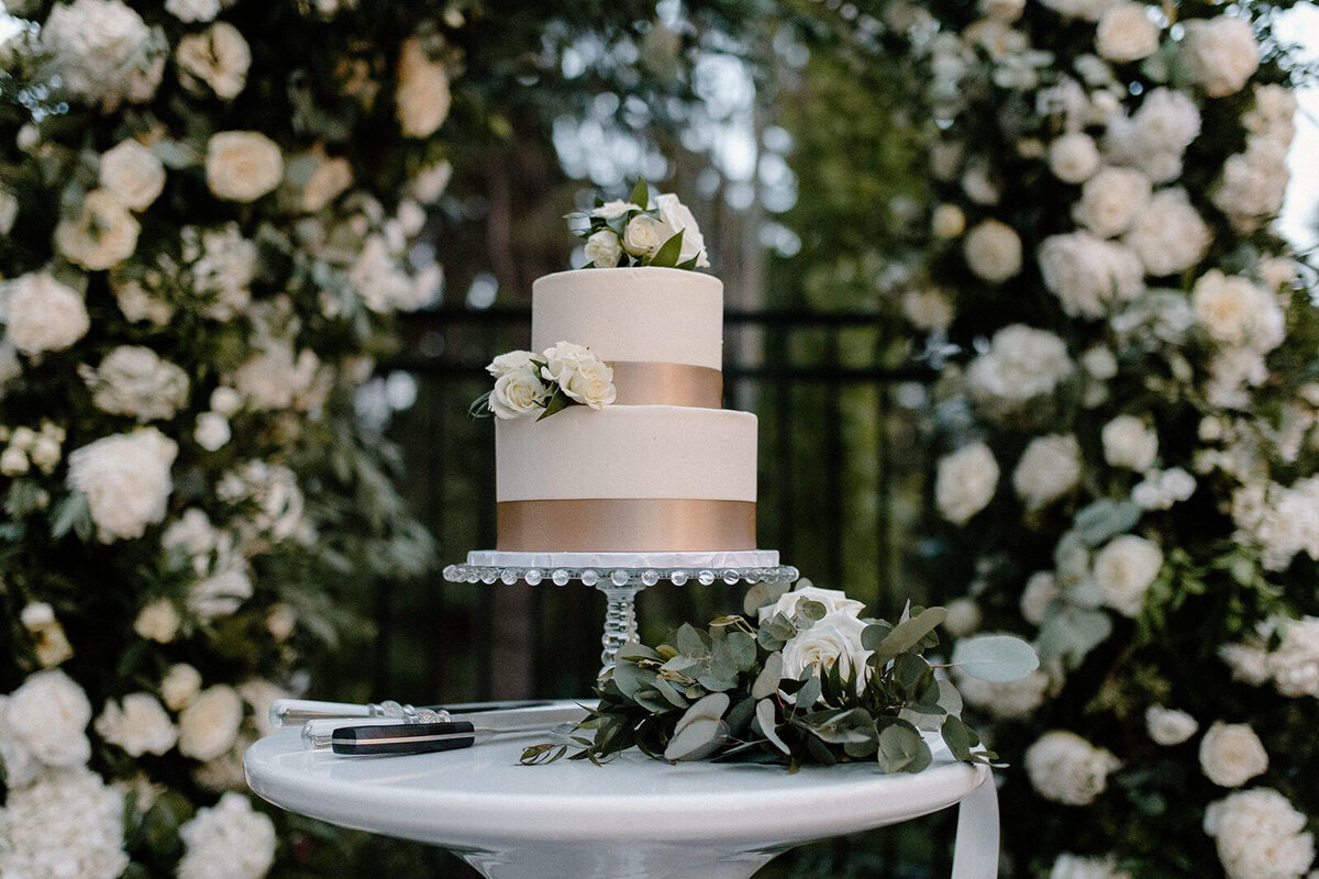 Gorgeous two-tiered wedding cake, surrounded by white roses, , captured by Nikki Collette, featured on the Brontë Bride Wedding Vendor Guide.