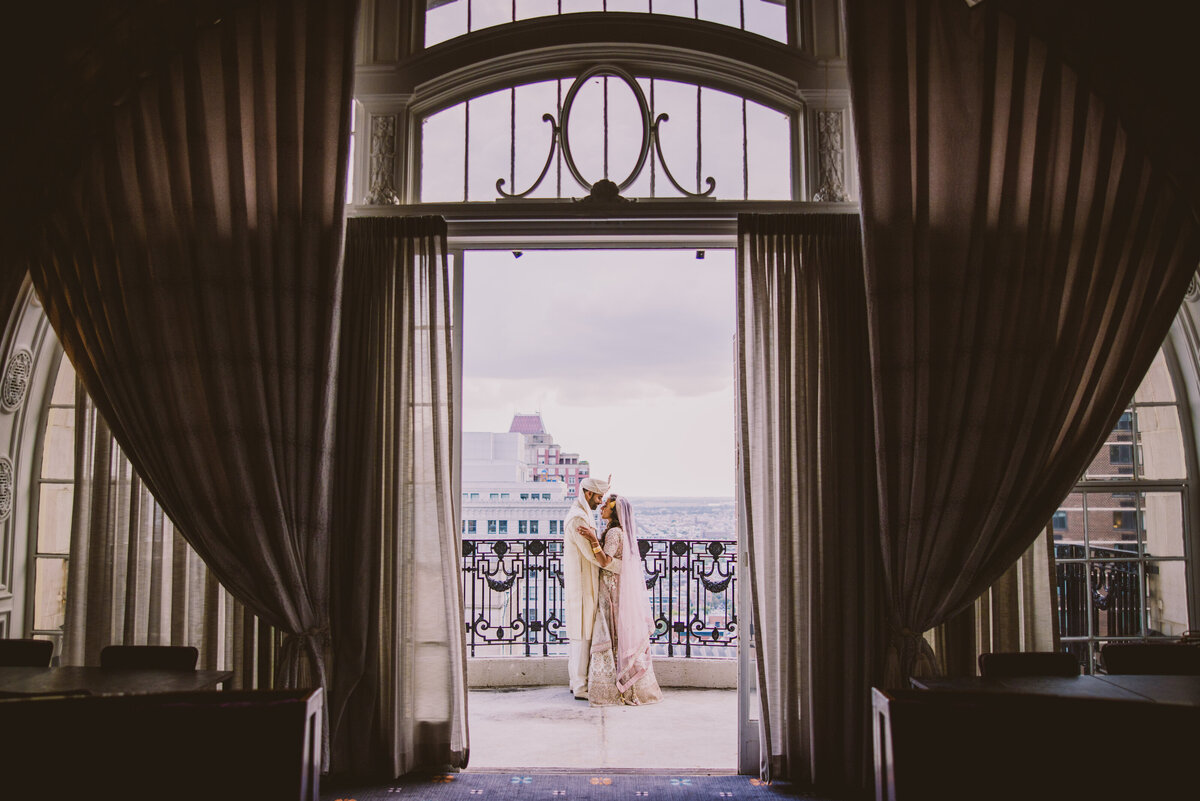 A pakistani and bengali bride and groom standing on the balcony of the bellevue hotel in philadelphia on their muslim wedding day