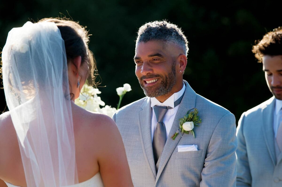 a groom smiles at a bride during the wedding ceremony