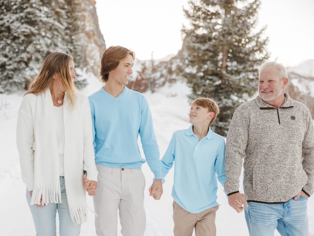A happy family with 2 teen boys hold hands while hiking a snowy pass