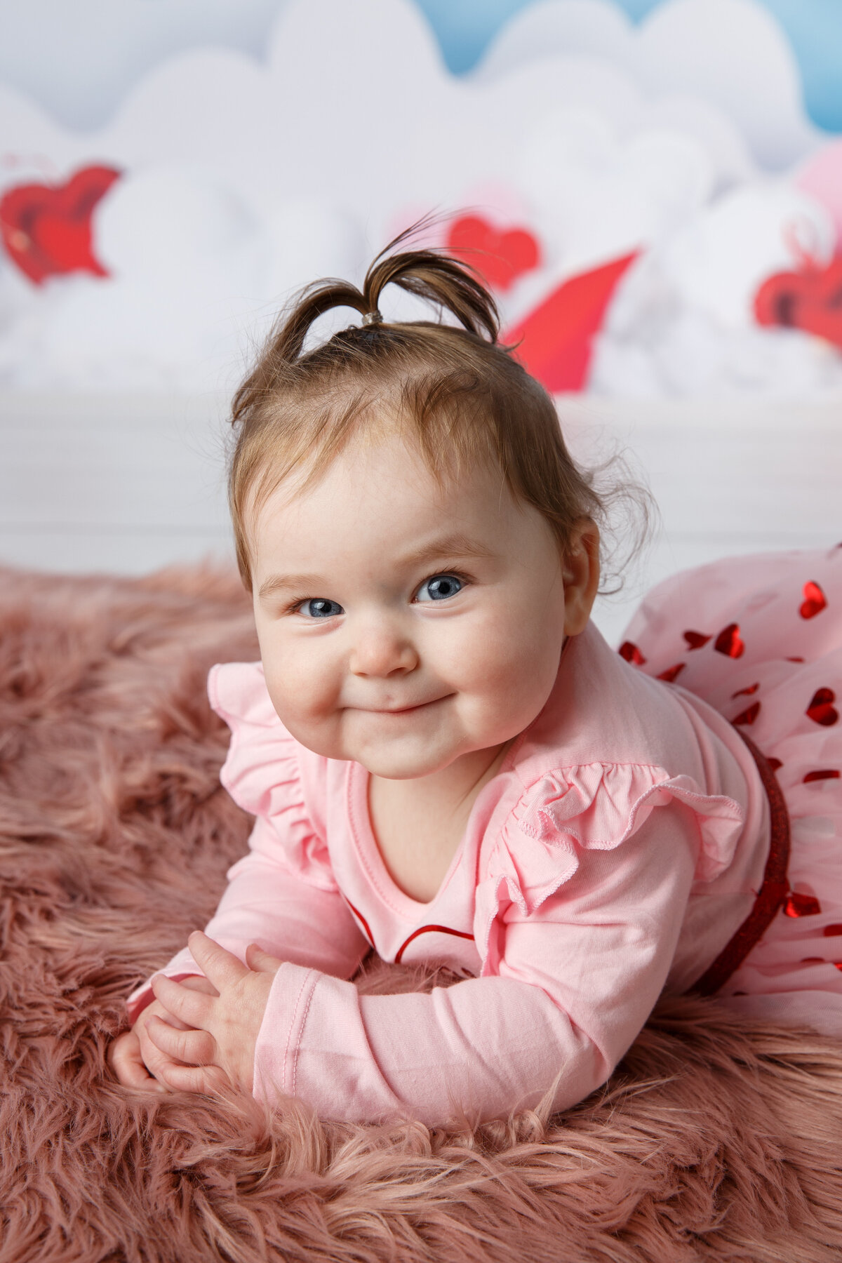 Portrait of a six month old baby girl smiling at the camera and wearing a pink shirt