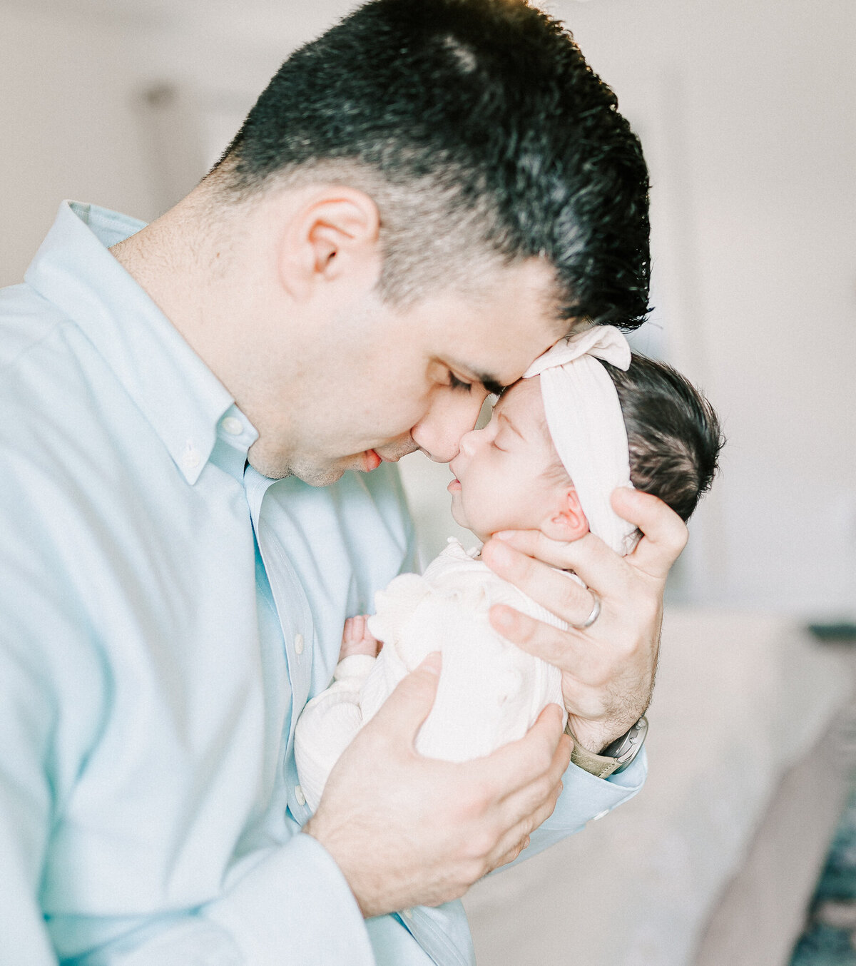 Heartwarming father-daughter moment in a natural light newborn photography session. A dad tenderly cradles his baby girl, showcasing the deep bond and love between them.