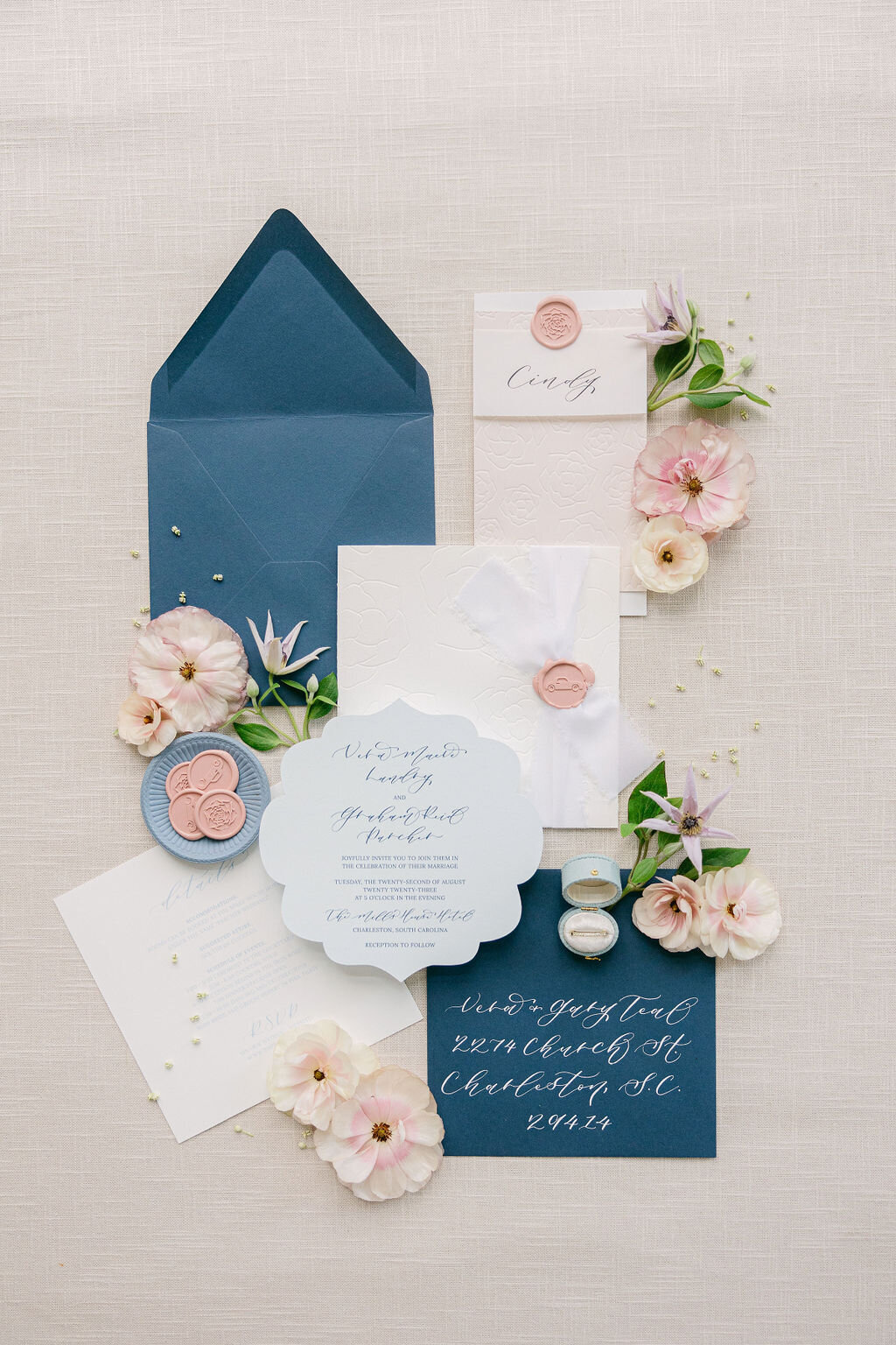 Dusty-blue and blush wedding invitation suite with wax seals, silk ribbon, and pastel florals—styled flat-lay for a Charleston celebration, captured by luxury wedding photographer Amia Marcell.