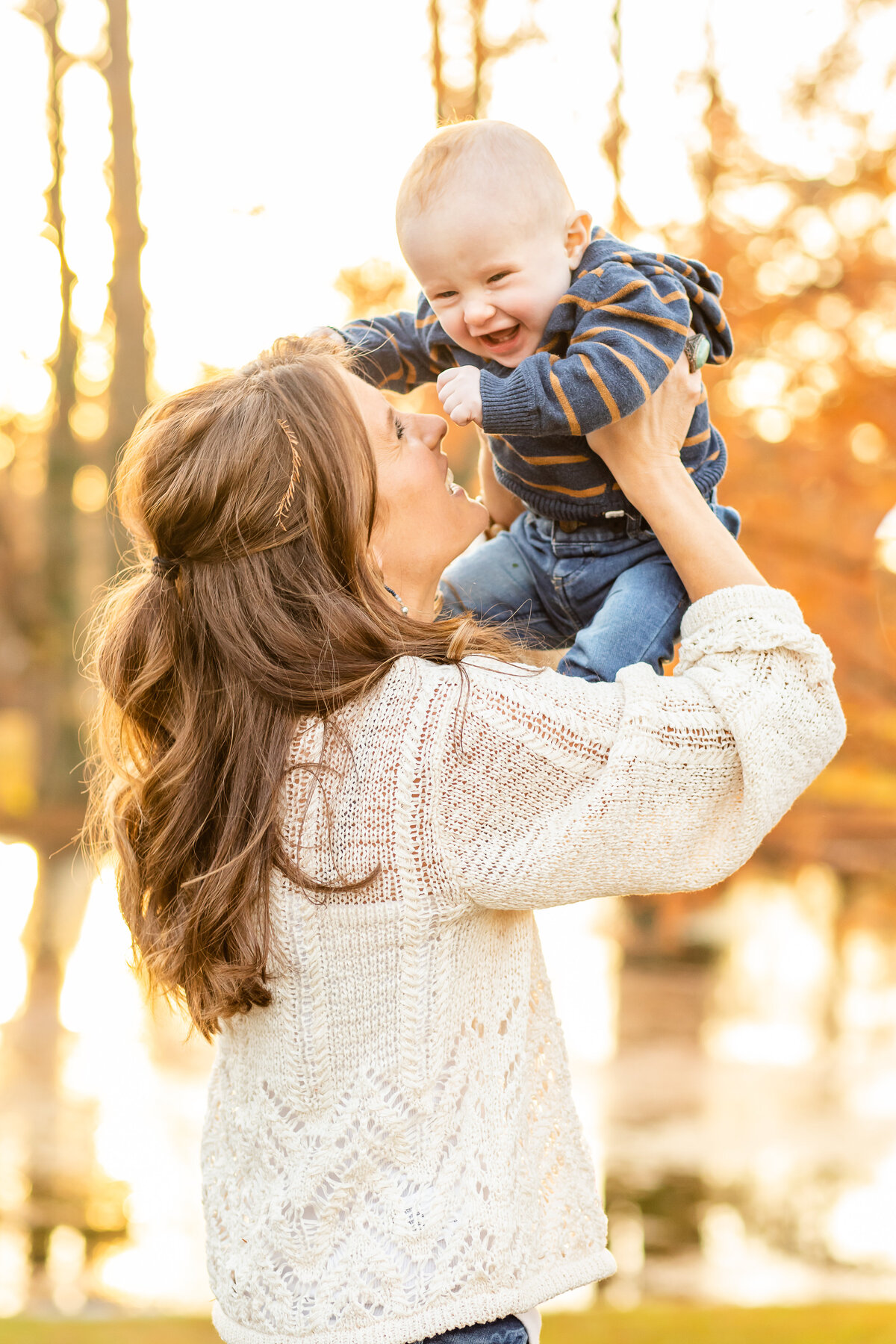 Mom tossing baby boy into the air with golden fall leaves and pond backdrop