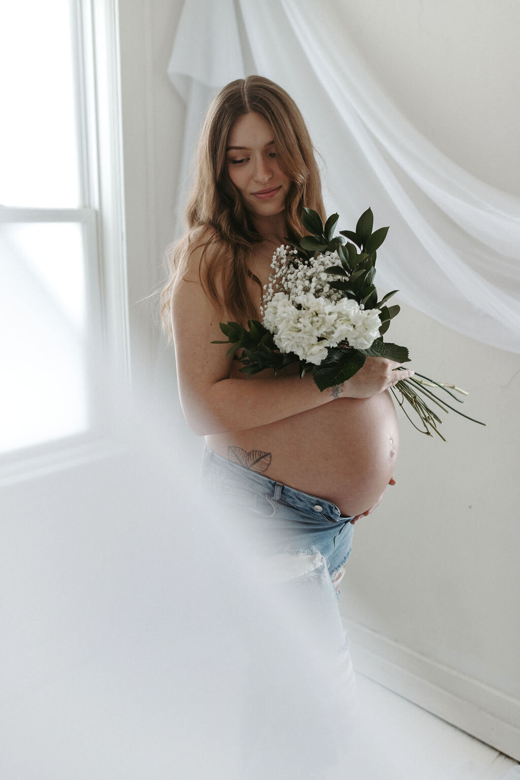 Pregnant woman holding flowers to her belly during a studio maternity session