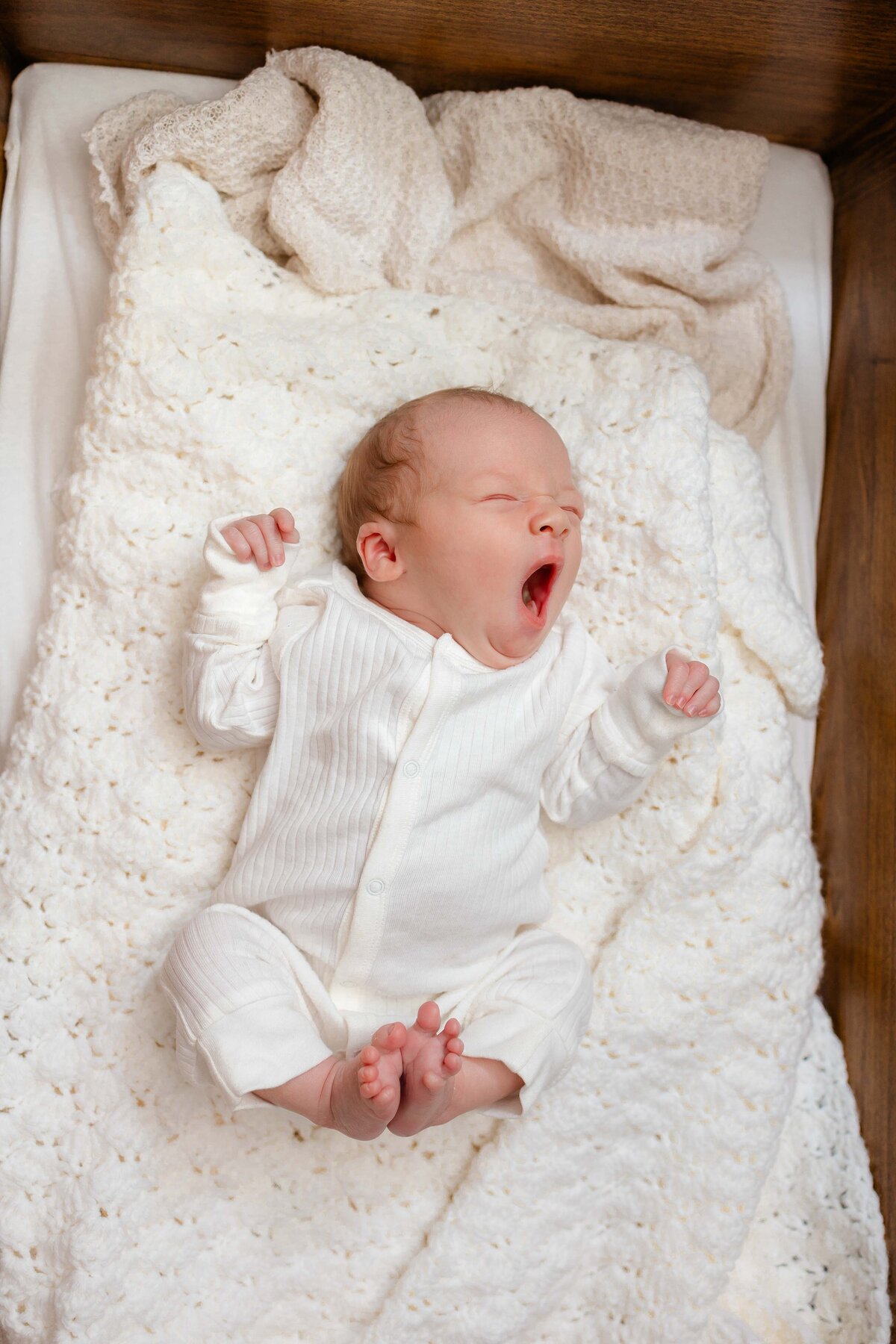 Newborn boy dressed in a white oneie yawning on a white blanket in Savannah, Ga