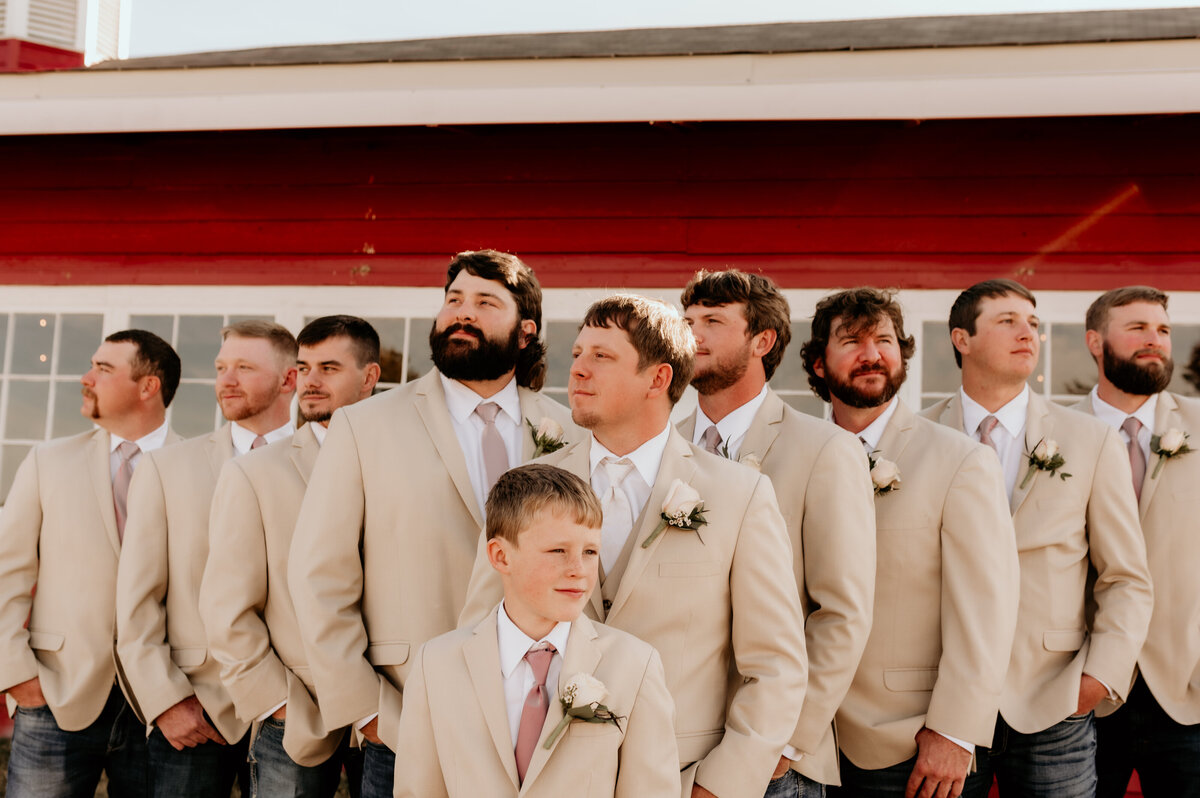 groom and his groomsmen standing outside in a line while looking off to the distance