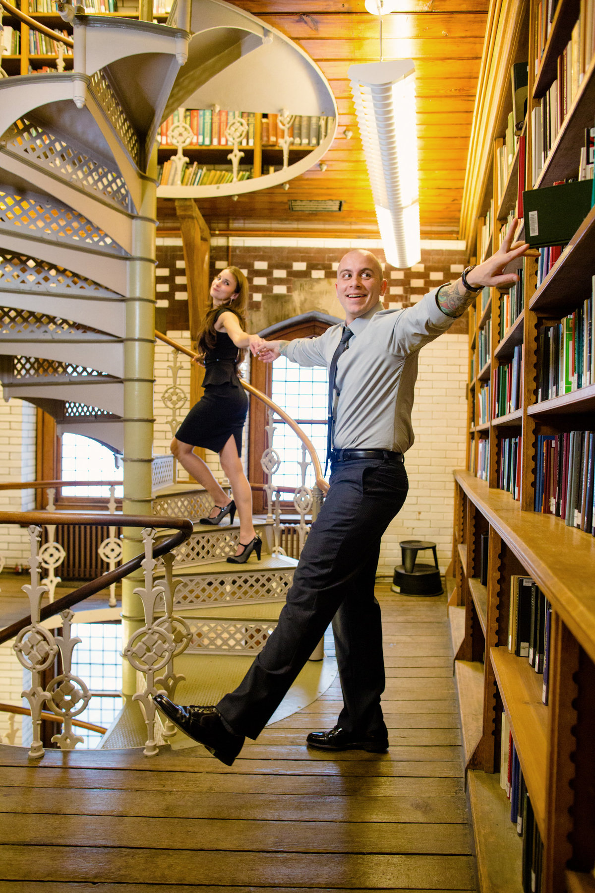 An engaged couple captured in a quirky and fun moment during their engagement session at the Lehigh University Library, surrounded by shelves of books and an atmosphere brimming with character.
