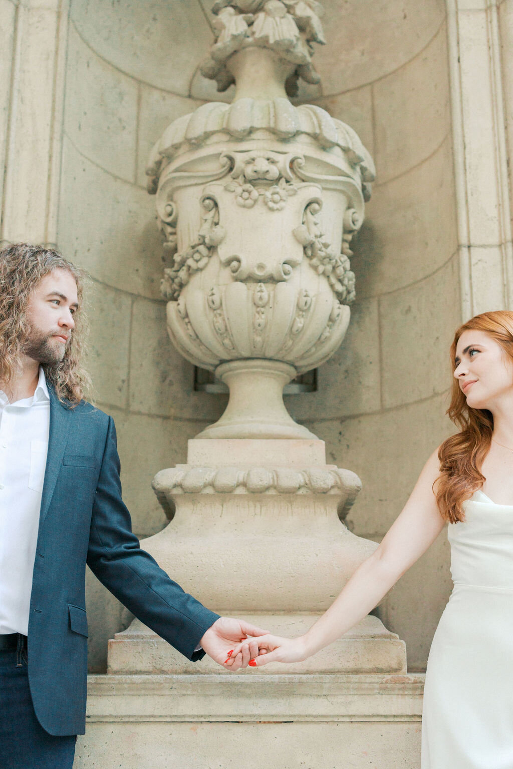 Bride and groom hold hands by stone urn at Swan House