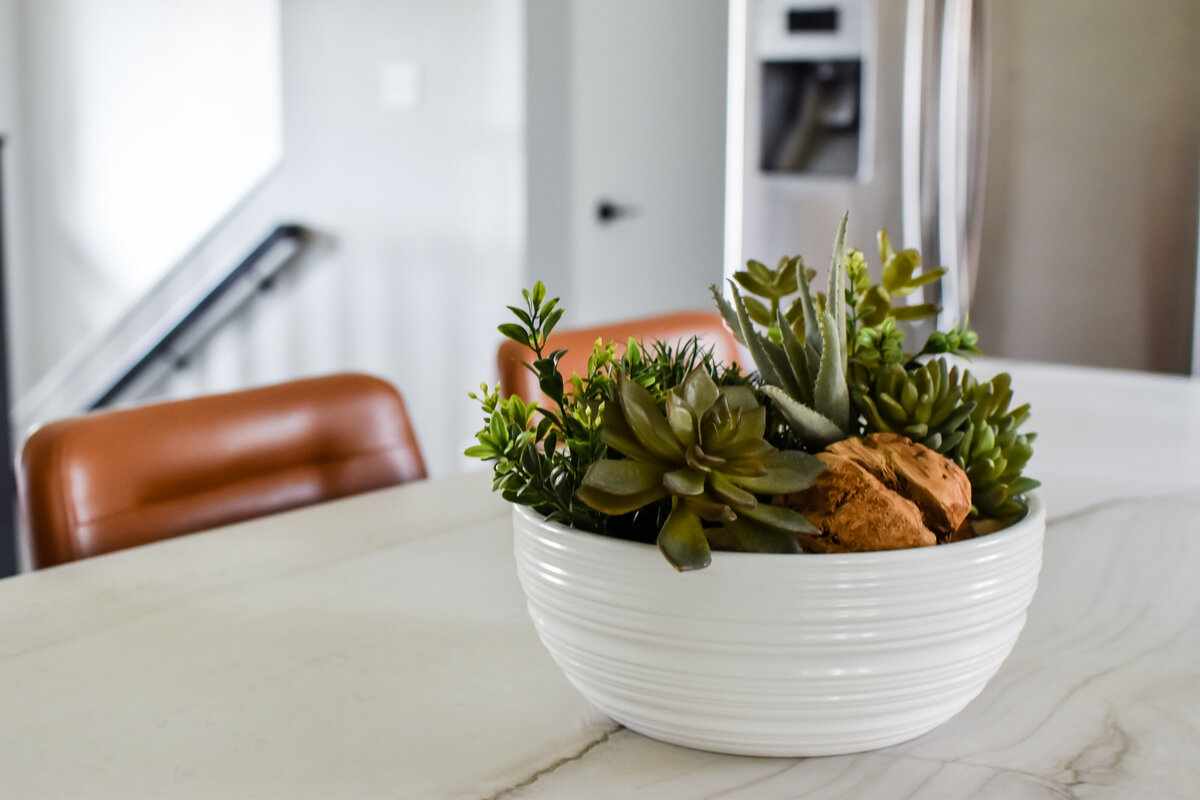 A bowl of plants sits on a large white kitchen island