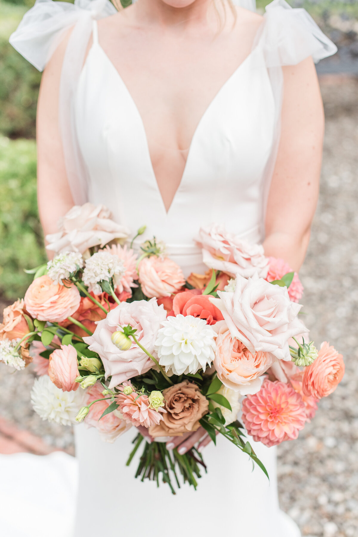 bride holding bouquet of roses dahlias and ranunculus in peach and blush color