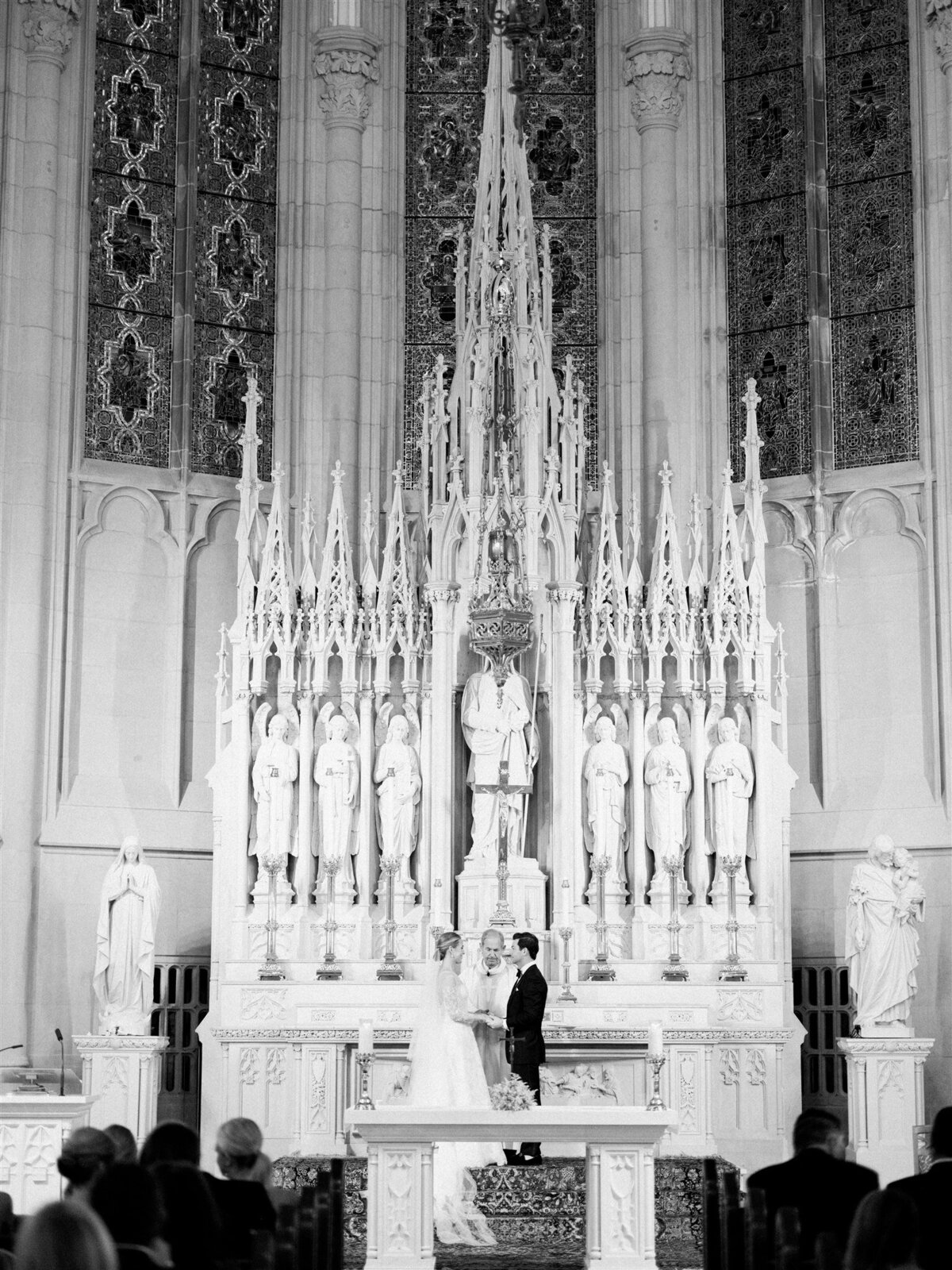 A black and white photo of the bride and groom at the alter holding hands during the ceremony. 