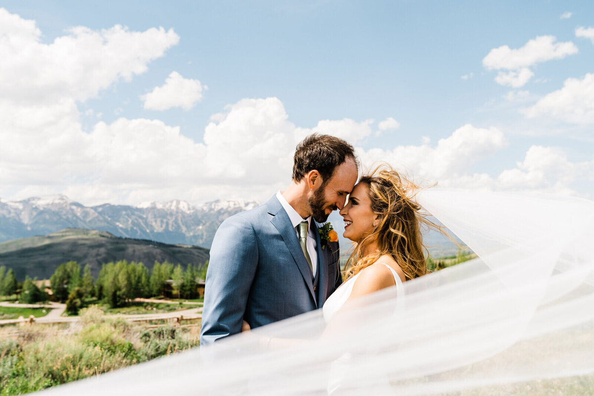 A bride's veil blows in the smiles at her groom on her wedding day near Grand Teton National Park