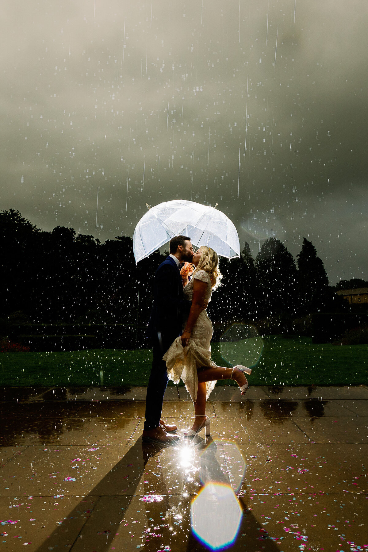 Bride and groom stood kissing under an umbrella in the rain at Utopia, Broughton Sanctuary