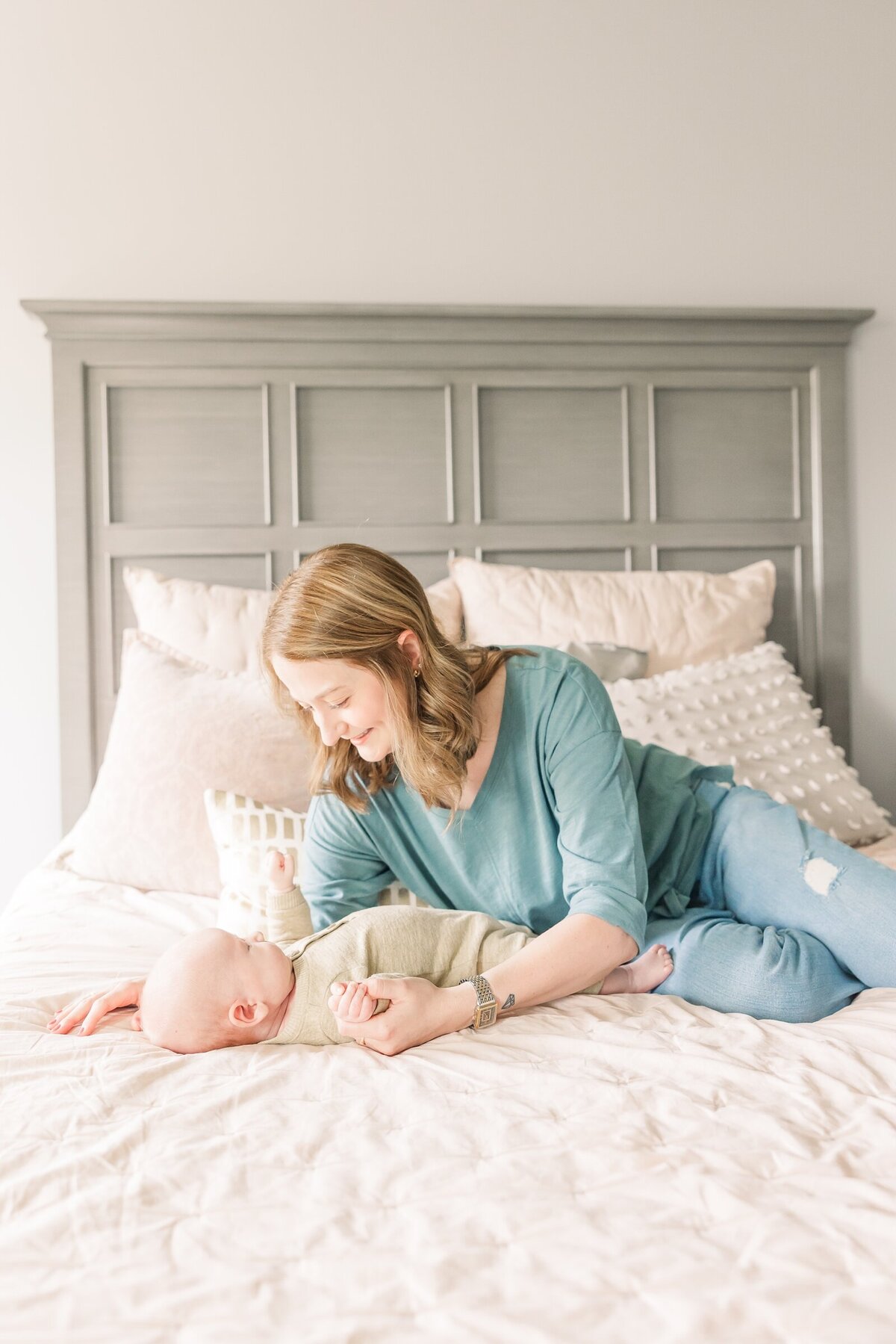 Mom laying on a bed and gazing down towards newborn baby during an Ohio newborn session