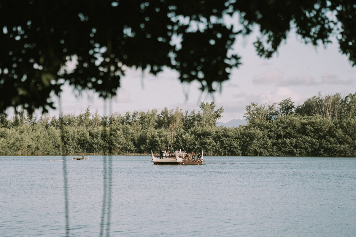 Distant view of a Kualoa Ranch boat through the trees