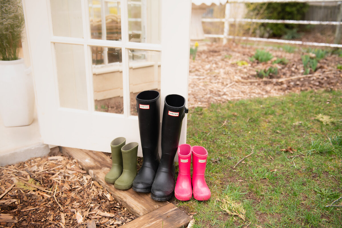 A charming lifestyle detail photo of a set family rain boots outside the floral greenhouse setup during a spring session in Dundas, Ontario at All Who Wander Flower Farm.