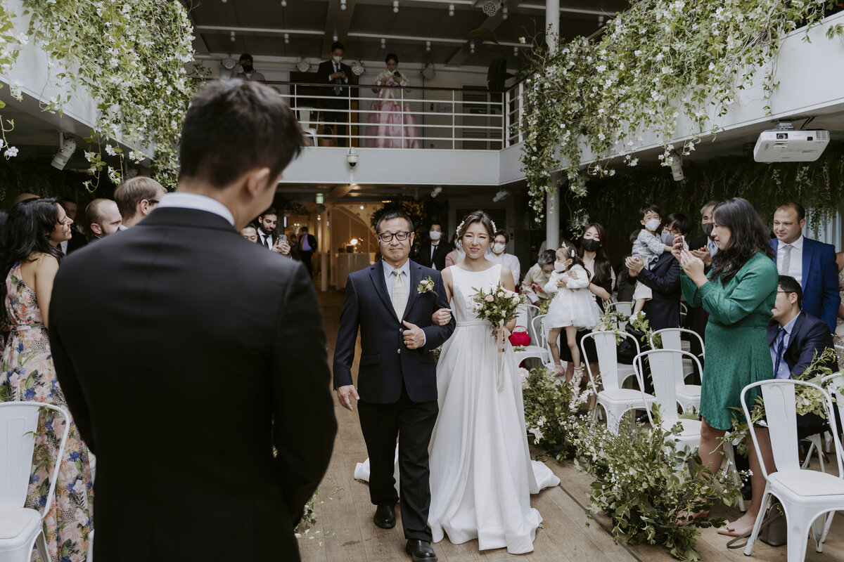 the bride with her father walking towards the groom and the guests celebrating it