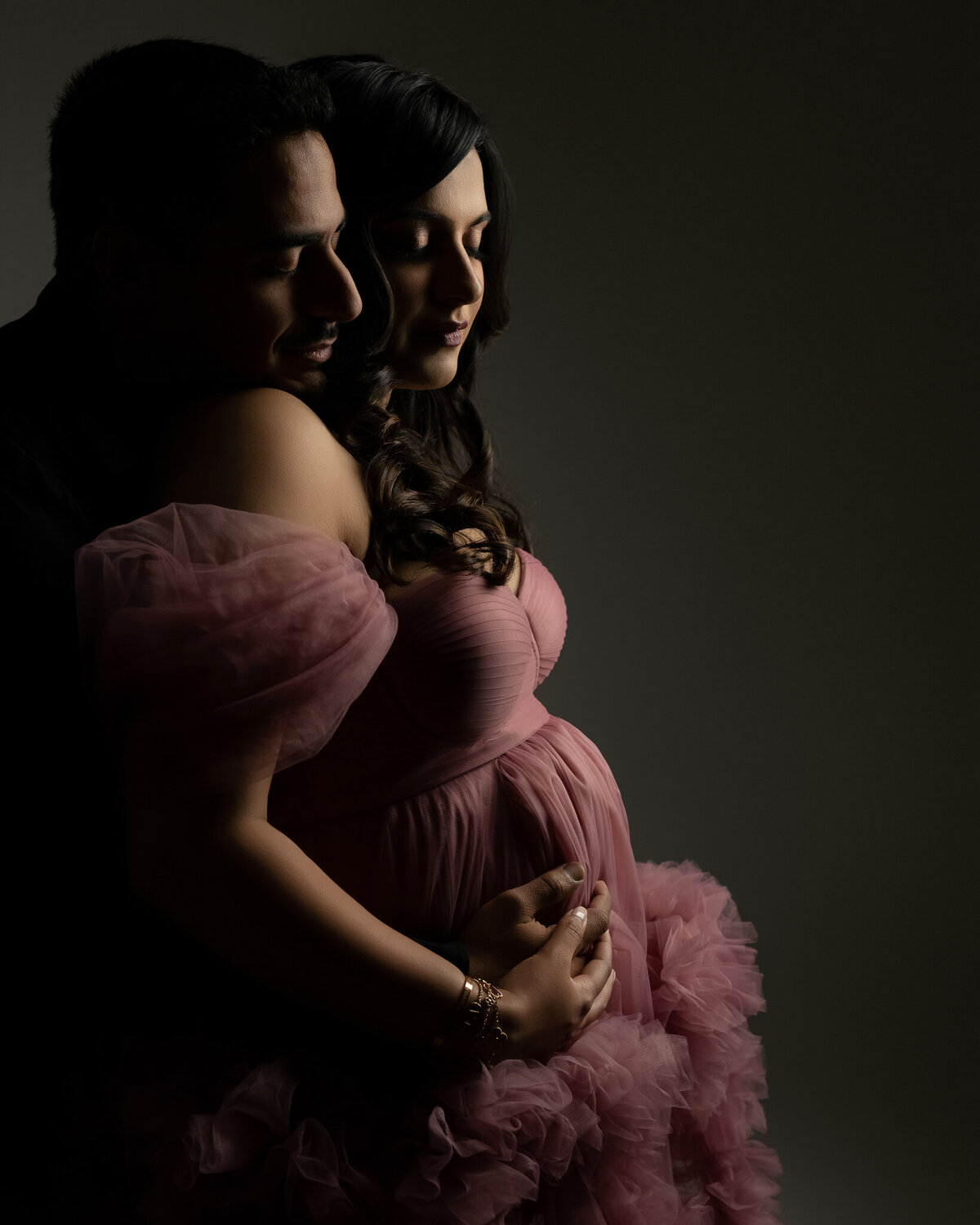 Studio maternity portrait of an expecting couple in a romantic pink gown, taken by a Leander maternity photographer.