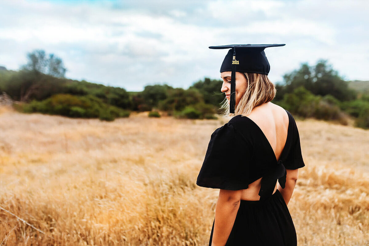 College graduate woman in a golden field with graduation cap and dress.