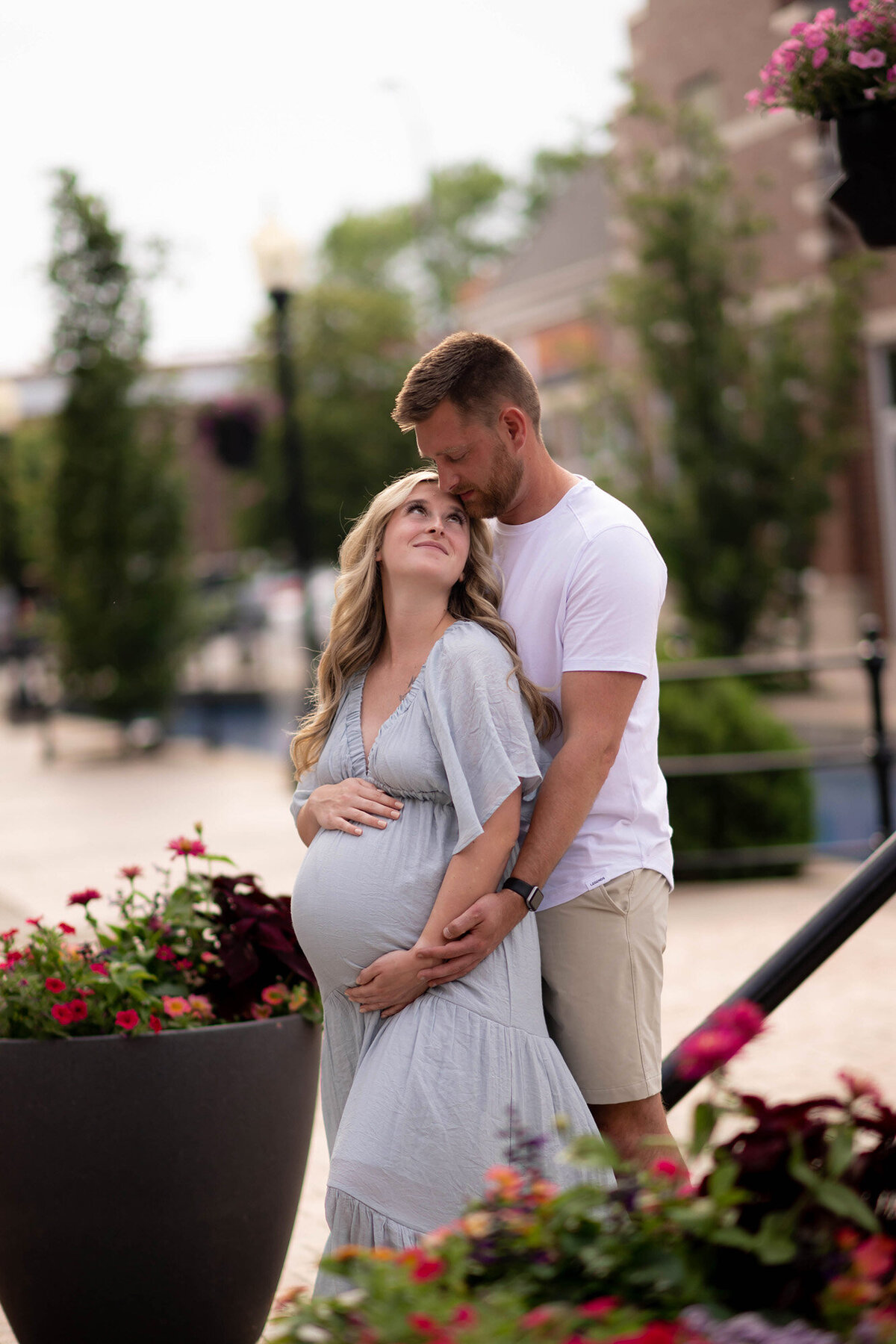 A smiling expecting couple cuddles while standing among flowers in a park