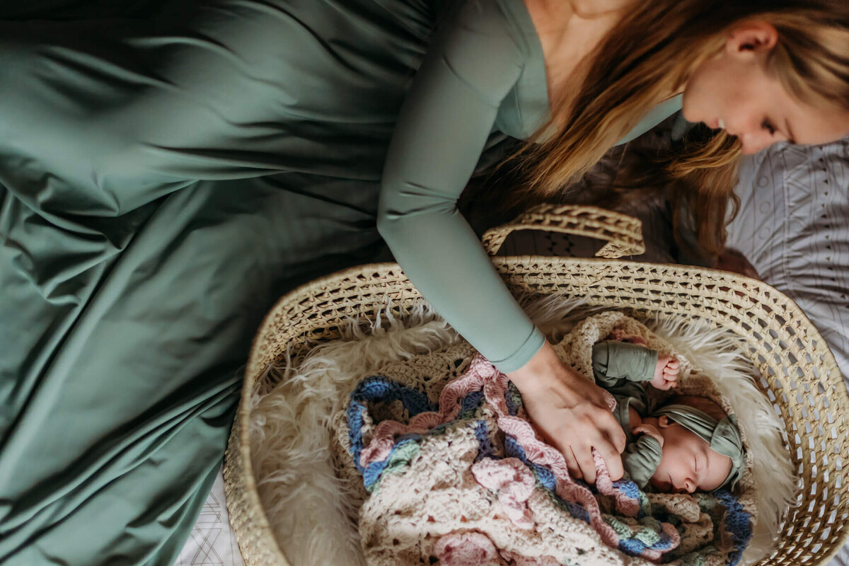 mom in green maternity dress tending to baby on bed