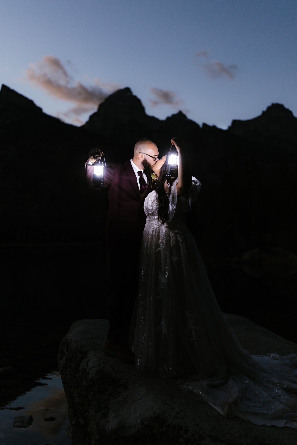A couple kissing and holding lanterns on a rock at Taggart Lake below the Grand Teton