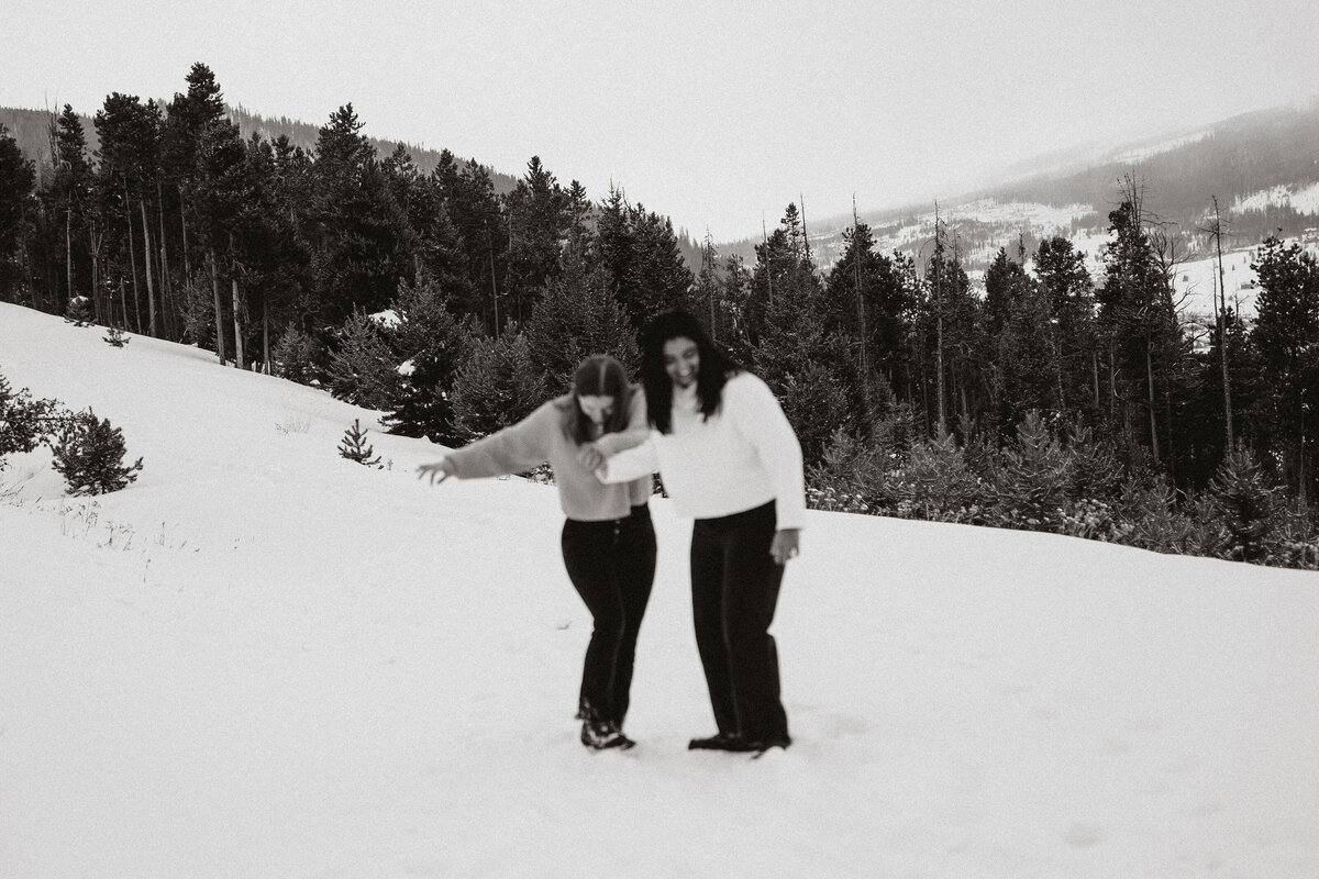Couple laughs and holds hands while playing in the snow during Sapphire Point engagement.