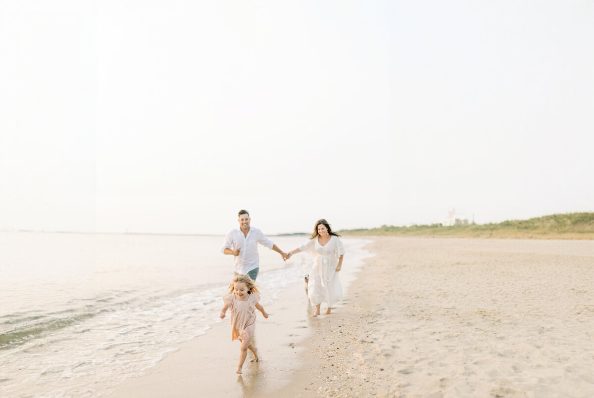 Mom and dad run down the beach behind their young daughter during sunset portrait session