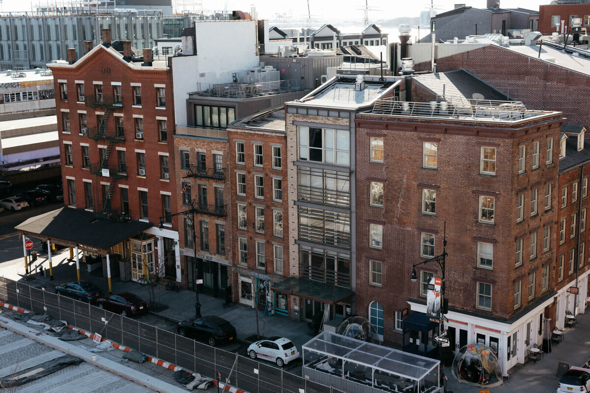 A block of five red-brick buildings with cars underneath.