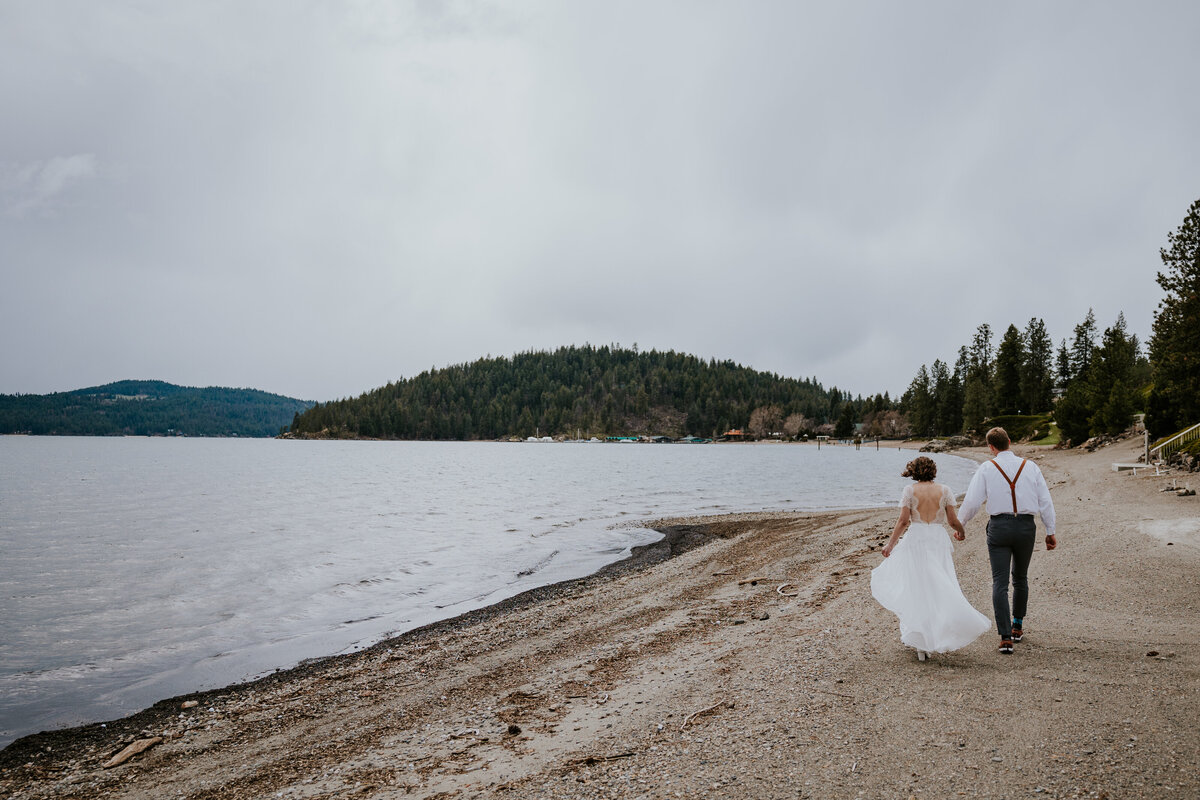 Bride and groom walk along the beach of lake Coeur d'Alene.