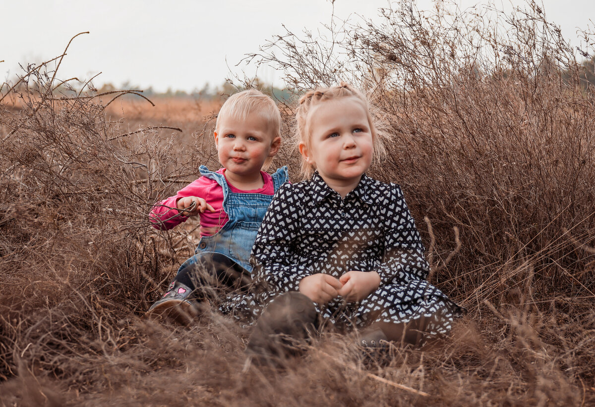 Twee zusjes zitten in het lange gras op de heide.