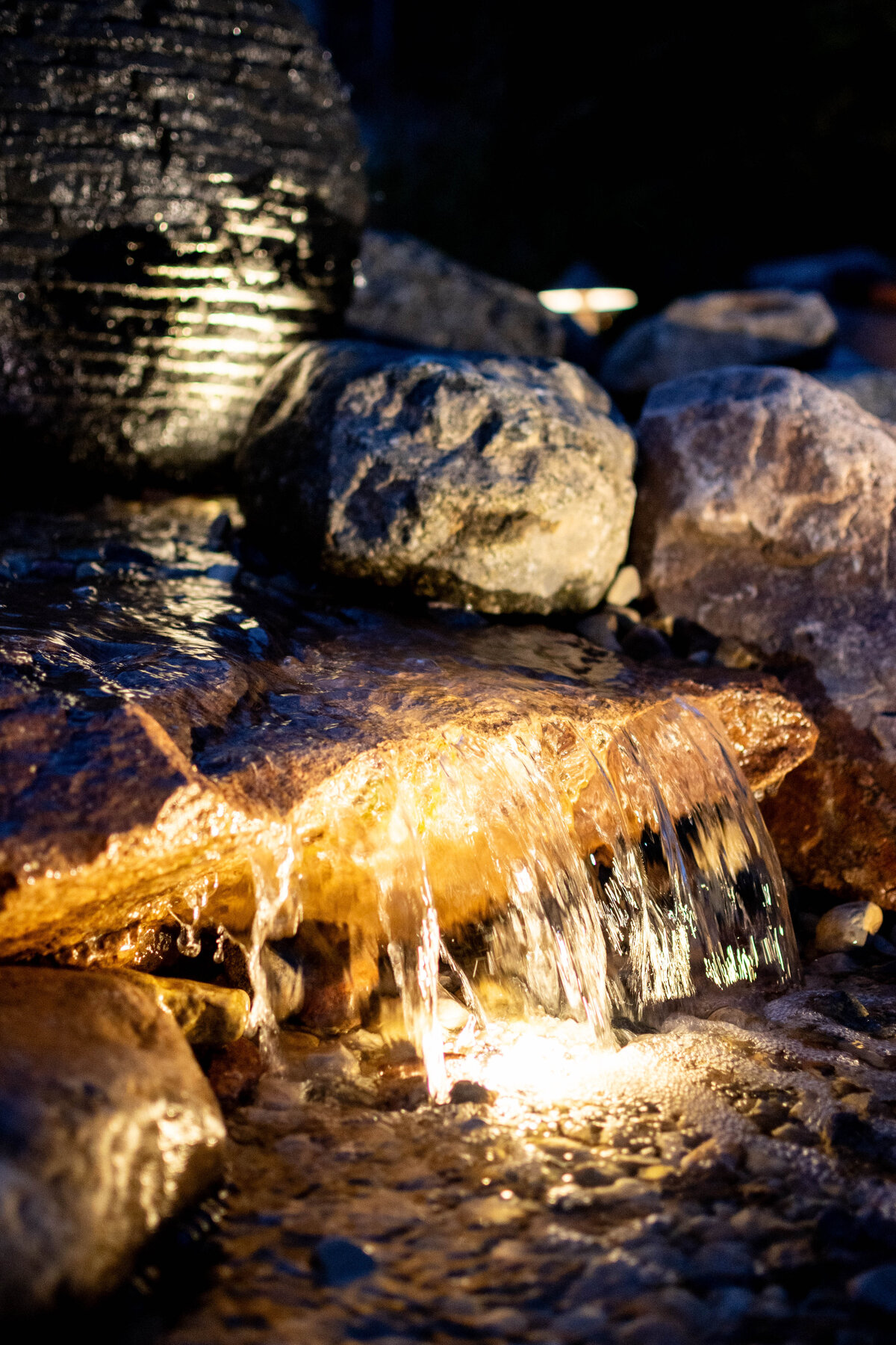 Waterfall flowing over edge of stone lit up at night