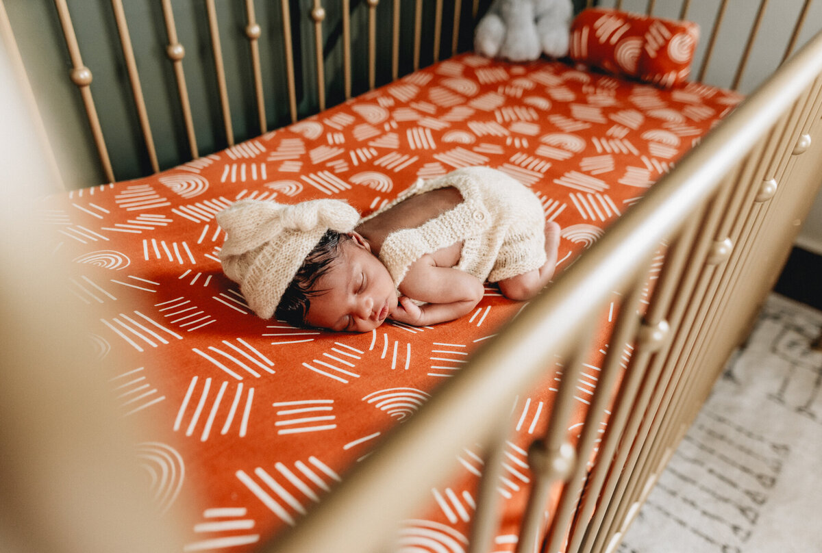 Infant photographer capturing newborn baby sleeping in a crib.