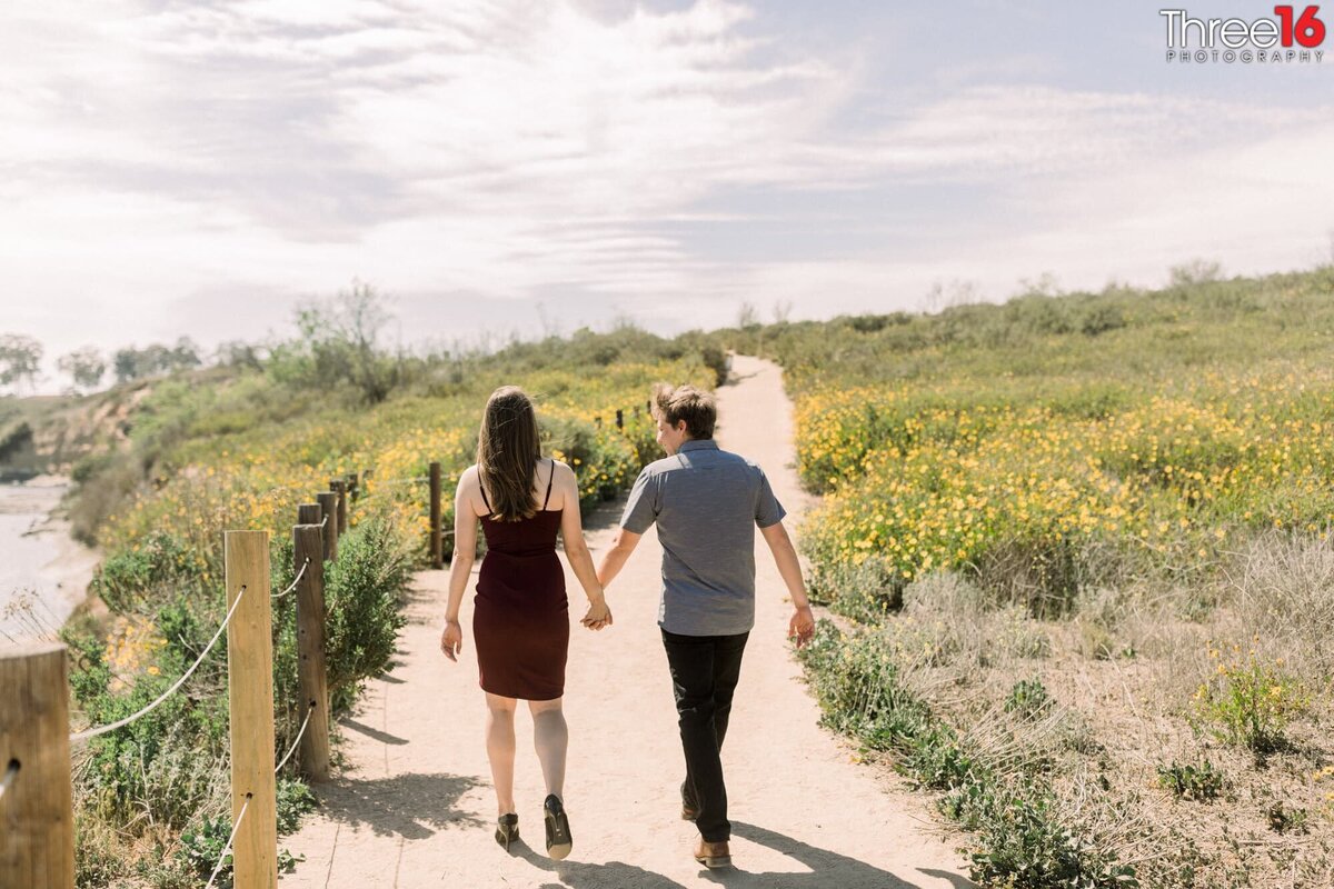 Engaged couple walk a Upper Newport Bay Nature Preserve trail holding hands