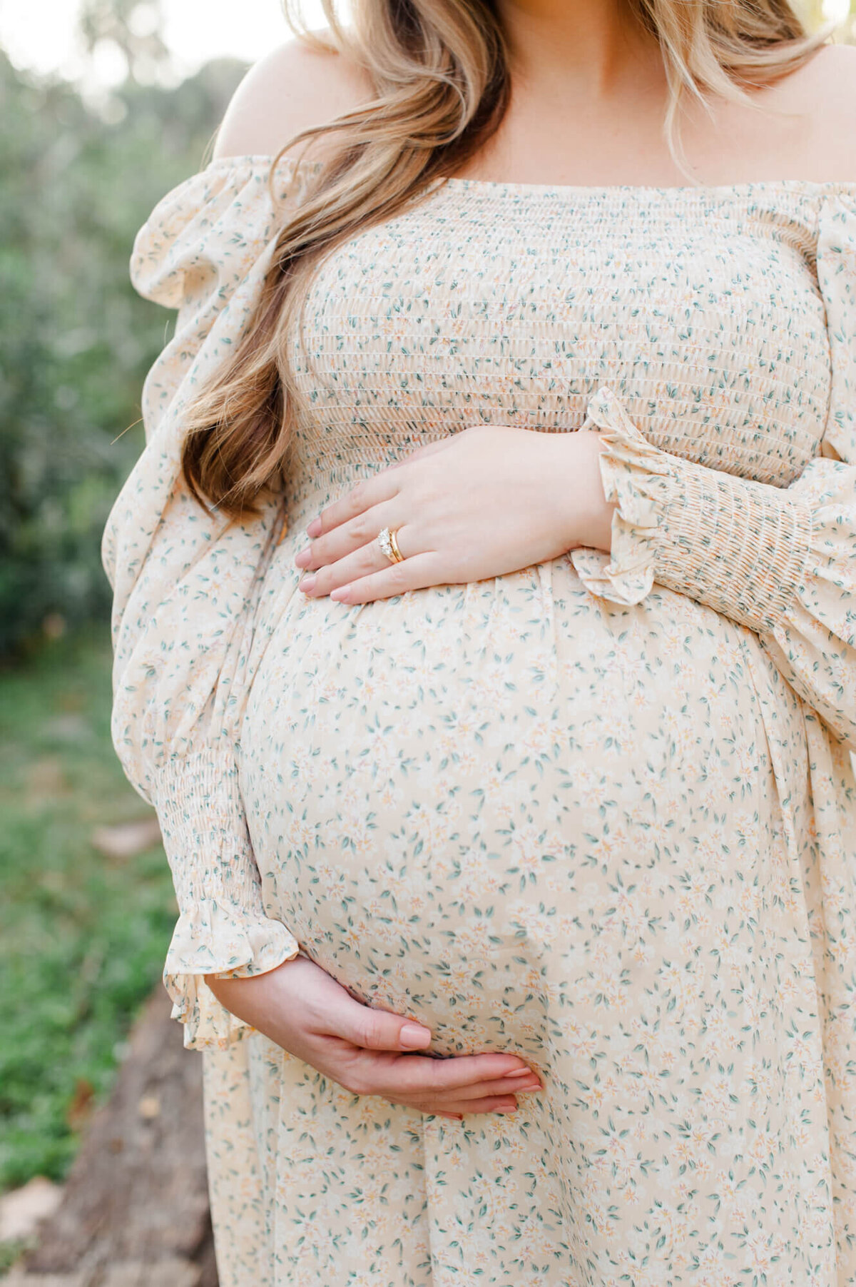 close up of mom holding her belly while wearing a neutral floral dress