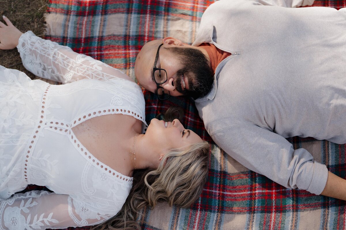 Couple lying on a plaid blanket, gazing at each other with smiles