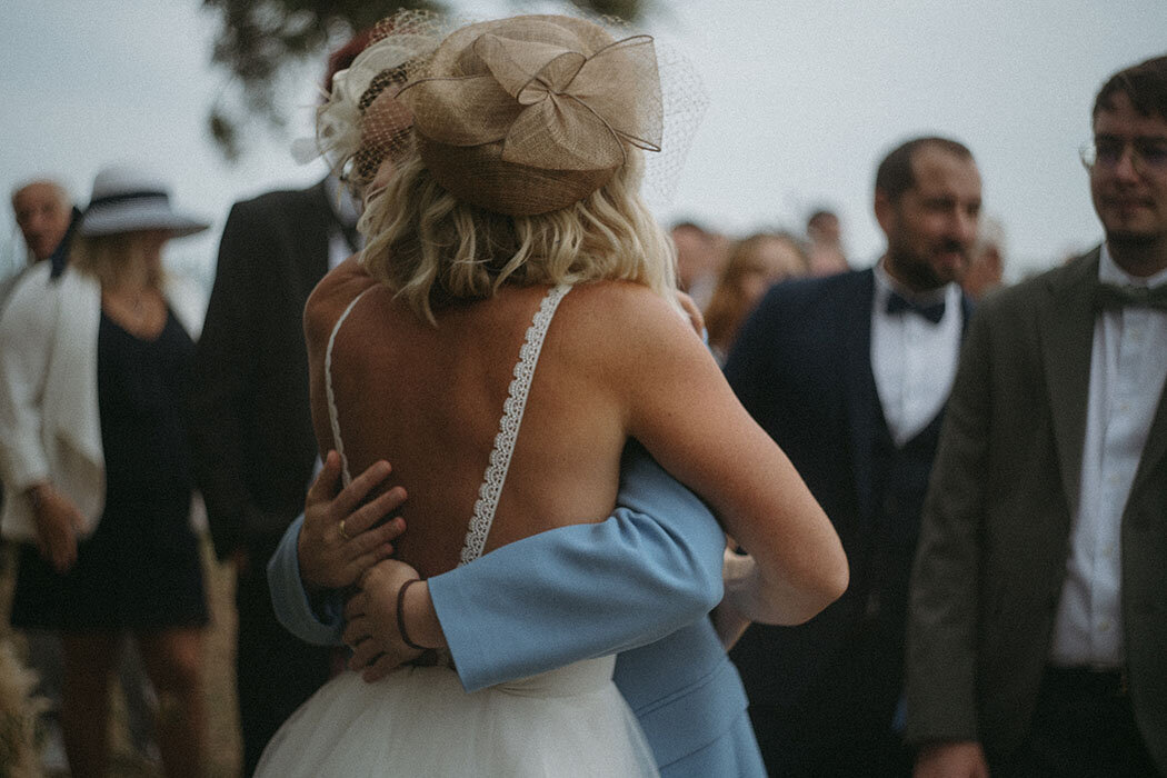 Mariée de dos enlaçant un invité en costume bleu. Par Kamescop, photographe et vidéaste mariage.