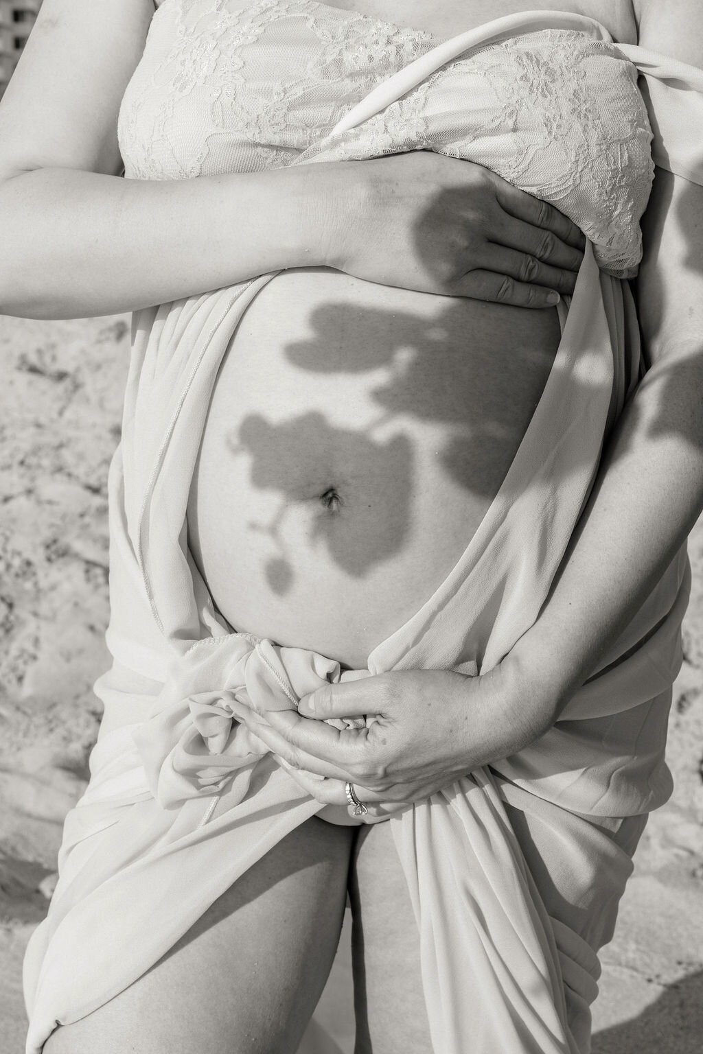 Close-up of a pregnant belly with an orchid flower shadow cast across it during a beach maternity session in Miami.