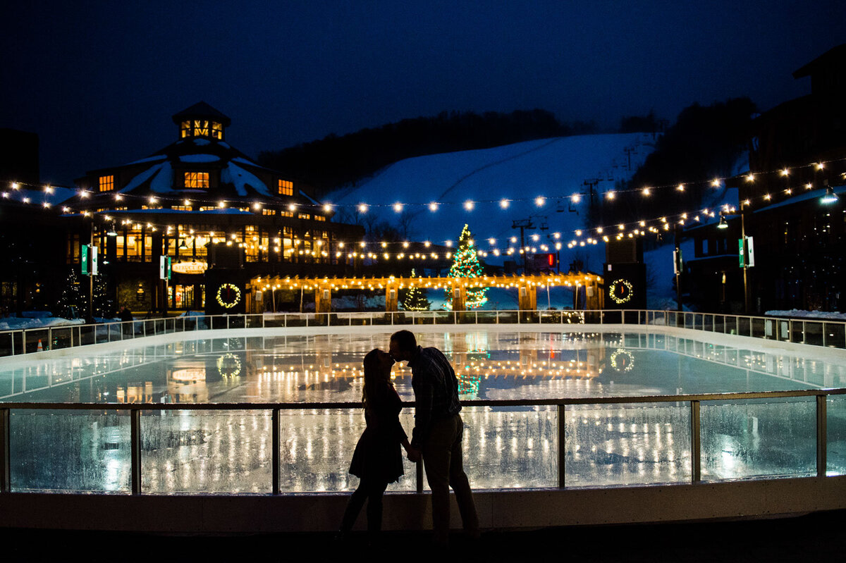 silhouette of couple kissing in front of ice rink at spruce peak stowe mountain lodge vermont christmas lights