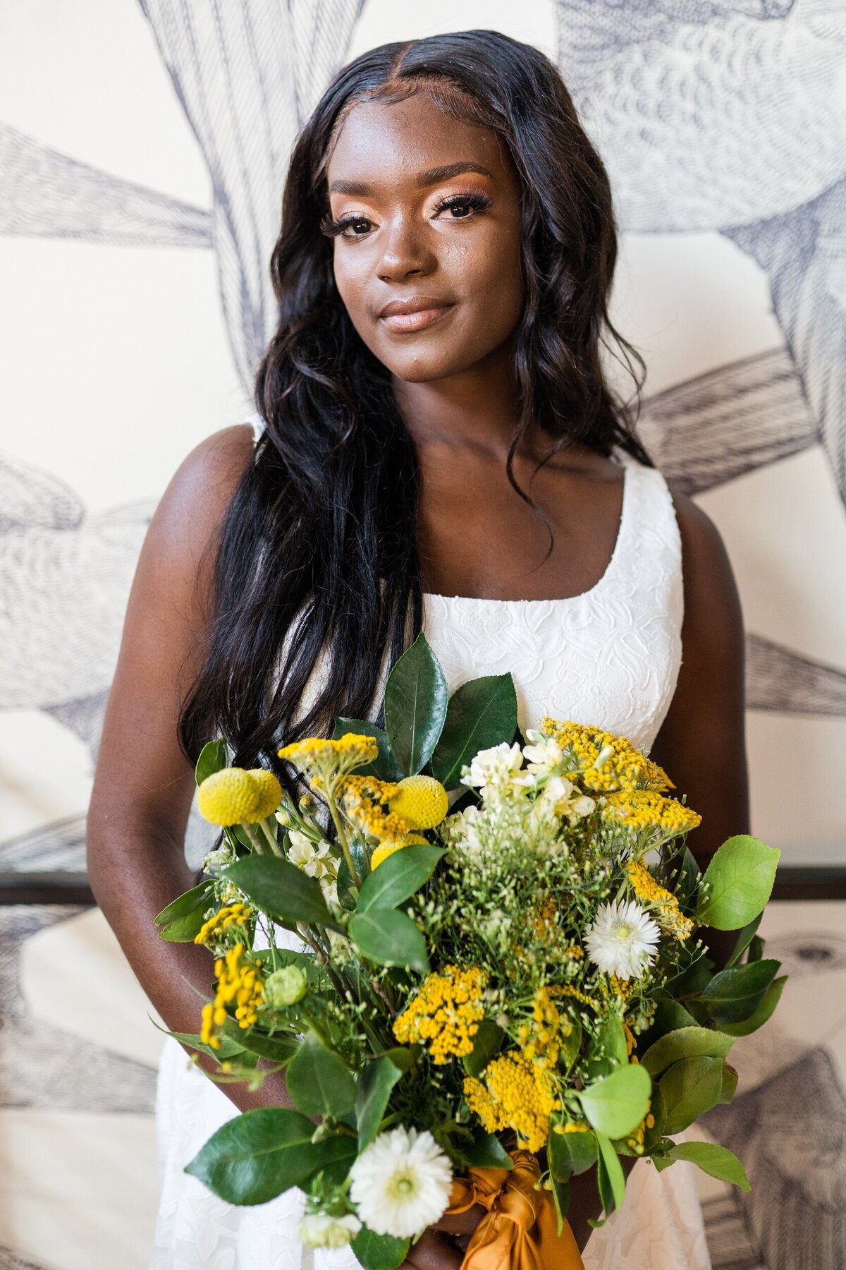 Bride looks confidently at the camera while holding a mustard yellow and green bouquet at Whitaker and Atlantic wedding venue in Raleigh, NC.