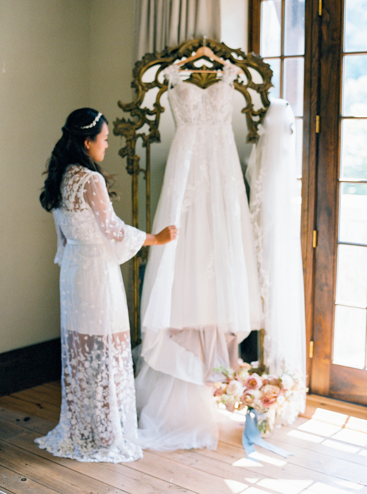 Bride admiring lace wedding gown hung on ornate mirror during getting ready at Castle Ladyhawke.